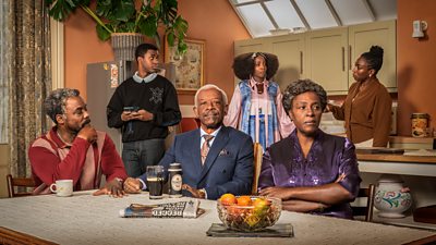 Six members of the Walker family in a kitchen. The protagonist, Barrington Jedidiah Walker, sits at a dining table and looks directly to the camera. 