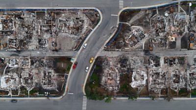 Aerial shot of shells of burned houses with a few cars on the street in between