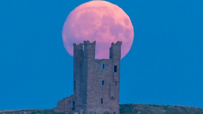 The moon appears large and orange above the castle. The sky is a dusty blue colour.