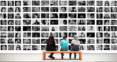 Three people look at a wall of photographs