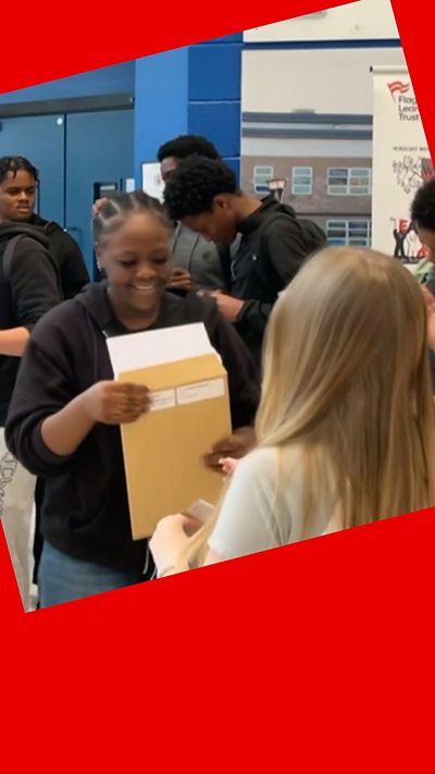 A student smiles as she pulls her GCSE results out of a brown envelope