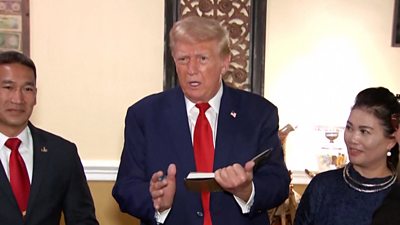 Donald Trump is seen talking to reporters while holding a book in his hands.