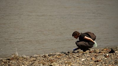 Women bends down to inspect Thames riverbed