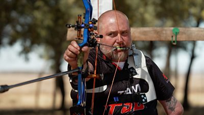 Shaun Anderson lines up a shot using a blue bow with a trigger release held in his mouth