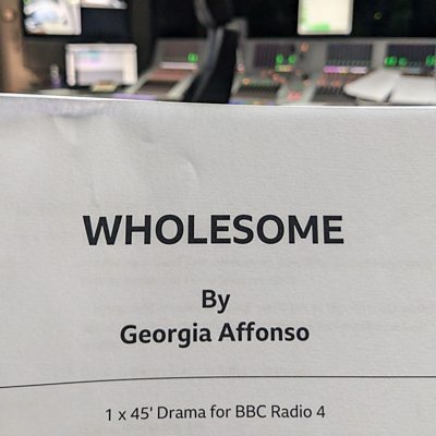 The front cover of the 'Wholesome' paper script held in front of a sound desk in studio