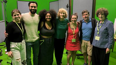 Seven members of the production team and cast for Wholesome standing in a line with their arms around each other in studio 