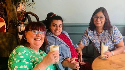 Sarah Wiles and Carissa and her mother are seated at a dining table, they are all holding hands and smiling toward the viewer