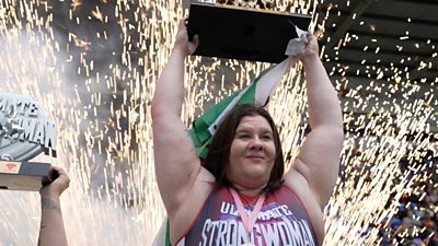 Rebecca Roberts lifting up a trophy and Welsh flag with fireworks going off behind her