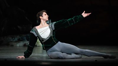 Reece Clarke performs on stage in a green velvet top and grey ballet tights.