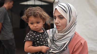 A mother holding her child speaks to journalists