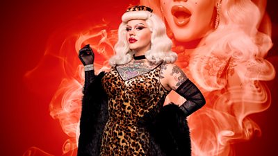 Drag Queen Lill in a leopard print strappy dress, black sheer long gloves and black fur piece draped on her arms. 50s style hair with a leopard print hat and a black choker. Red smoke effect in background with partial image of Lill in the smoke