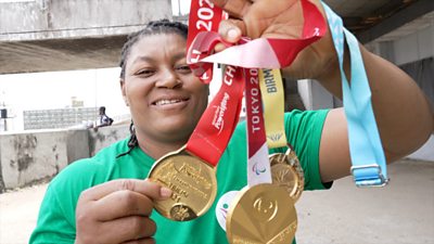 Foleshade Oluwafemiayo in green t-shirt holds up three gold medals