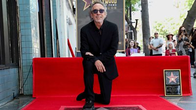 Tim Burton is kneeling down by his star in the Hollywood Walk of Fame