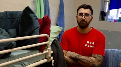 Man in red top stands in prison cell