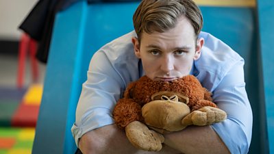 Robert Spearing (Harry Lawtey) rests his chin on a teddybear that he cuddles to his chest. 