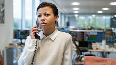 Harper (Myha’la) holds a phone to her ear as she stands in an empty office. 