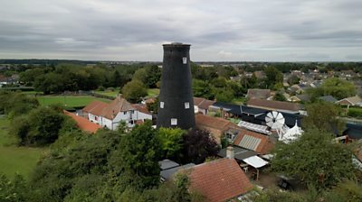 Drone shot of a mill with the cap removed. The white cap is next to the black mill standing among red-roofed buildings.