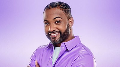 JB Gill smiles to the camera wearing a purple shirt over a light blue t-shirt