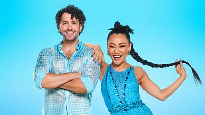 Shayne Ward and Nancy Xu pose together dressed in blue. Nancy leans one arm on Shayne's shoulder as he stands with his arms crossed.