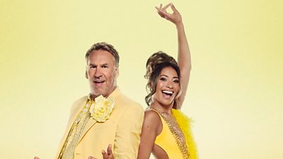 Paul and Karen stand back to back, smiling in bright yellow outfits