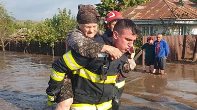 Firefighter carries old woman on his back in the middle of a street river