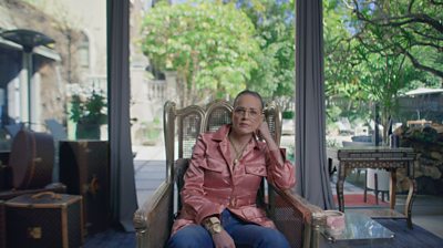 Sharon Stone leaning on her hand in a chair with big windows and a garden behind her