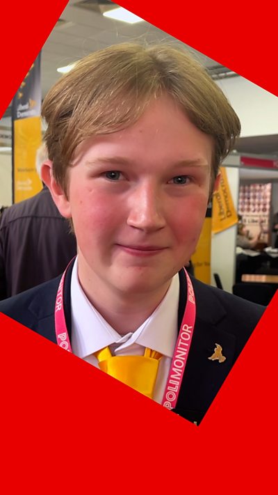 A man with short brown hair - he wears a suit with a yellow tie