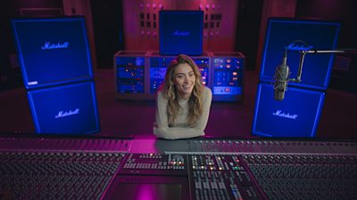 Paris Jackson leaning on a soundboard in a recording studio smiling 