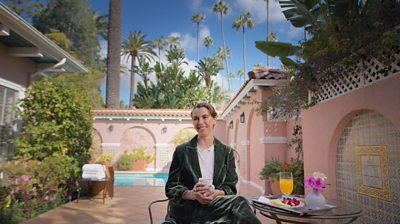 Naomi Wilding sitting on a chair in a courtyard with a pool in the background. 