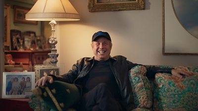 Todd Fisher sitting on a sofa in a living room smiling widely 