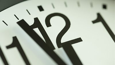 A very Close up image of a clock face with the minute hand close to the number 12