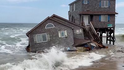 A house is seen half collapsed into the waves