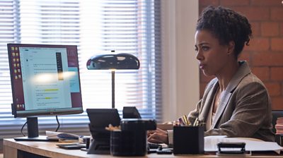 Nina Toussaint-White sitting at a desk looking at a computer screen with a concerned look on her face 