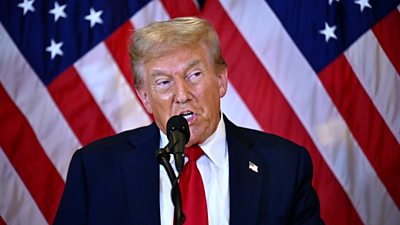 Donald Trump speaking at Trump Tower with American flags behind him