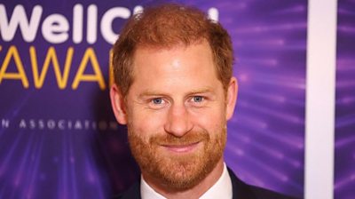 Prince Harry poses for a photograph in front of a purple banner