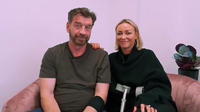 Nick Knowles and Luba Mushtuk sit on a pink sofa with a pair of crutches