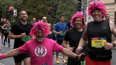 Three male runners wearing bright pink wigs smile at the camera.