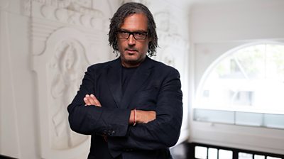 David Olusoga in a white building with ornate walls with his arms crossed looking to the camera