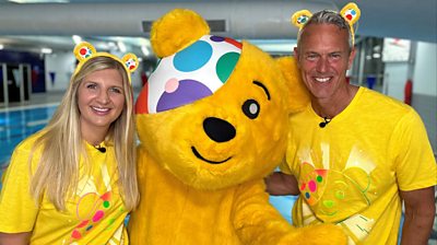 Rebecca Adlington, Pudsey and Mark Foster smiling to camera. Rebecca and Mark are wearing Pudsey ears 