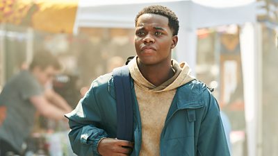 Close up of Jaheim (Josh Tedeku) carrying a backpack outdoors on a sunny day. 