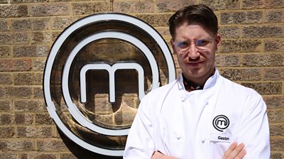 joins Gaston, standing in front of MasterChef M, looking towards the camera and wearing a MasterChef-branded shirt