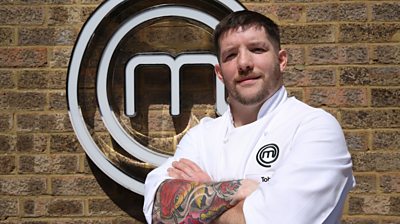 joins Toby, standing in front of MasterChef M looking at the camera and wearing a MasterChef branded shirt