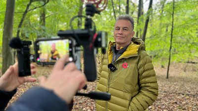 behind-the-scenes shot of Chris Peckham being photographed in the woods with a camera in the foreground