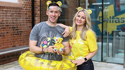 Connor Phillips and Holly Hamilton smile for the camera wearing branded clothing for BBC Children in Need. Connor wears goggles and an inflatable rubber ring in reference to the 'mammoth challenge swim team' challenge. 