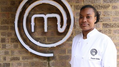 Woman wearing MasterChef branded t-shirt in front of the MasterChef logo smiles at the camera