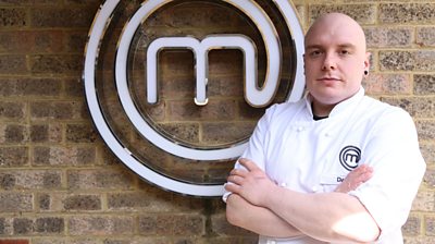 Man wearing MasterChef branded t-shirt in front of MasterChef logo looking at camera