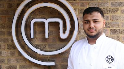 Man wearing MasterChef branded t-shirt in front of MasterChef logo looking at camera