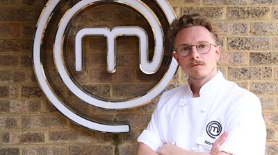 Man wearing MasterChef branded t-shirt in front of MasterChef logo looking at camera