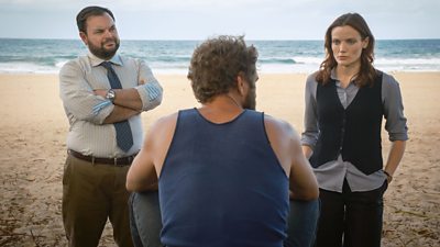 Detective SC Colin Cartwright (Lloyd Griffith) and DI Mackenzie Clarke (Anna Samson) stand on a beach speaking to a man whose back is turned to the camera