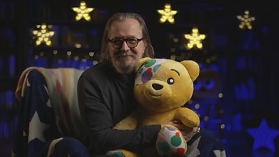 Gary Oldman holds a Pudsey the bear with stars in the background